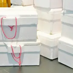 Stos białych, styropianowych opakowań z czerwono-białymi sznurkami. Idealne do transportu delikatnych produktów.