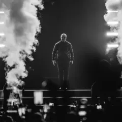 Pitbull na scenie, otoczony dymem i światłami, podczas koncertu.