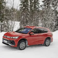 Czerwony Volkswagen Tiguan 5N pokonuje zasypaną śniegiem drogę w lesie.