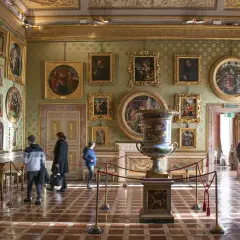 Interno di una sala del Palazzo Pitti, con opere d'arte alle pareti, un grande vaso e visitatori.