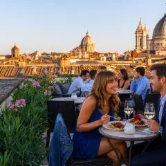 Coppia felice cena in uno dei ristoranti con vista Roma, con cupole e tetti all'orizzonte.