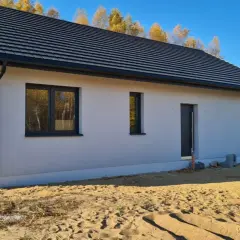 Nowy dom z szarym dachem i białymi ścianami, z oknami i drzwiami, w stanie surowym zamkniętym.