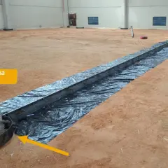 Instalación de una solera de hormigón con armadura metálica sobre plástico negro en interior de nave.