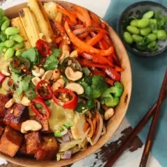 Kolorowa miska z ryżem, pieczonym tofu, warzywami i orzechami, obok pałeczki.
