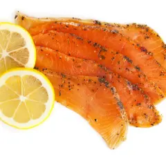 Skivor av gravad regnbåge med peppar och två citronskivor på vit bakgrund.