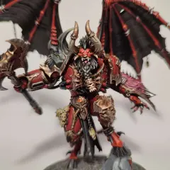 Groźny chaos daemon prince z czerwono-złotą zbroją, czarnymi skrzydłami i toporem.