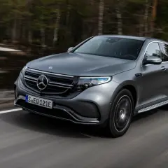 Szary Mercedes EQC jedzie po drodze wśród drzew.