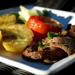 En tallrik med dubbelmarinerad oxfile, rostade potatishalvor, en bakad tomat och gröna bönor.