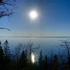 En solig dag för omberg vandring. Träd silhuetter mot en klarblå himmel och ett glittrande vatten.