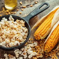 Pachnący, świeży popcorn w żeliwnej patelni, obok kolb kukurydzy i ziaren. Zastanawiasz się, ile kosztuje duży popcorn w Heliosie?