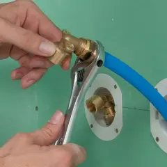 Installation d'un raccord pour l'arrivée d'eau de la douche. Une clé serre un coude en laiton sur un tuyau bleu.