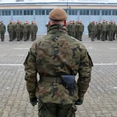 Żołnierze w mundurach polowych stoją na placu apelowym. To widok zza pleców jednego z nich, który jest gotowy do służby.
