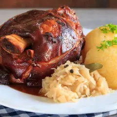 Knusprige Schweinshaxe mit Sauerkraut und Klößen, garniert mit Petersilie. Ein herzhaftes Gericht, das Appetit macht.