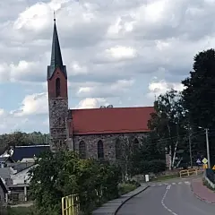 Kamienny kościół z czerwoną dachem i strzelistą wieżą to jedna z głównych atrakcji Sierakowic. Wokół widać domy i zieleń.