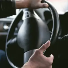 Manos sujetando el volante de un coche. La dirección del coche rota, indicando un giro o una maniobra.