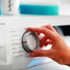 Dłoń kręci pokrętłem pralki, wybierając program. Szukamy cichej pralki, ile decybeli?