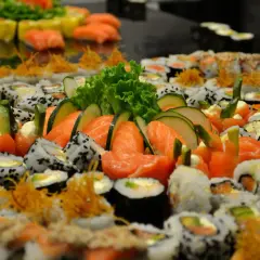 Mnóstwo sushi z łososiem, ogórkiem i sałatą. Wśród nich widać kawałki ryby maślanej, tworząc apetyczną kompozycję.