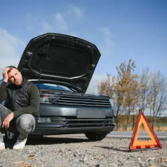 Zmartwiony mężczyzna przy awaryjnym samochodzie z otwartą maską. Obok trójkąt ostrzegawczy. Zastanawia się, jakie dokumenty są potrzebne do złomowanie auta.