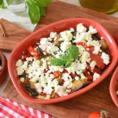 Pyszna pieczona feta z warzywami, podana w glinianym naczyniu, z dodatkiem świeżej bazylii i pomidorków.
