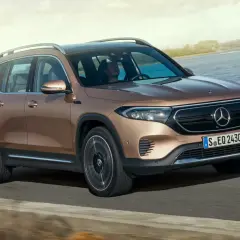 Brązowy Mercedes EQB jedzie po drodze nad jeziorem.