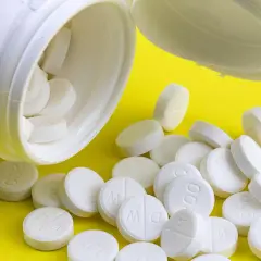 Białe tabletki, niektóre z napisem "200", wysypują się z białego pojemnika. Mogą zawierać tocopherol, cenny antyoksydant.