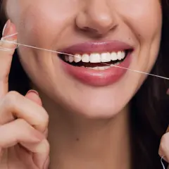 Uśmiechnięta kobieta używa nić dentystyczna do czyszczenia zębów. Dba o higienę jamy ustnej.