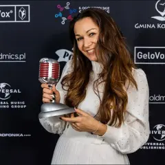 Uśmiechnięta kobieta z mikrofonem-statuetką. Jej stylizacja i nagroda sugerują, że to inspiracja dla tych, którzy chcą dowiedzieć się, jak zostać dubbingiem.