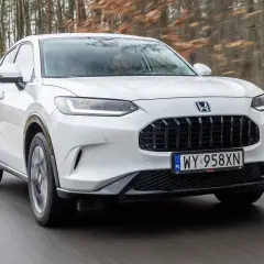 Biały Honda ZR-V jedzie po drodze wśród drzew.
