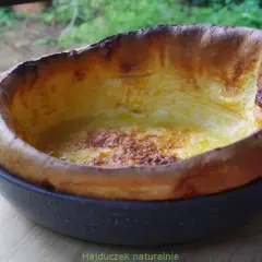 Puszysty, złocisty dutch baby, lekko przypieczony na brzegach, w okrągłej formie.