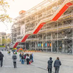 Widok na Centre Pompidou z czerwonymi schodami ruchomymi i ludźmi spacerującymi po placu.
