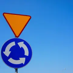 Znak A7 (ustąp pierwszeństwa) nad znakiem oznaczającym rondo. Niebieski okrąg z białymi strzałkami symbolizuje ruch okrężny.