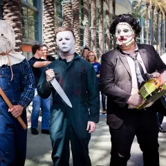 Trzech mężczyzn w strojach znanych postaci z horrorów: jeden z workiem na głowie i siekierą, drugi jako Michael Myers z nożem, trzeci jako Leatherface z piłą łańcuchową. Groźny slasher na konwencie.