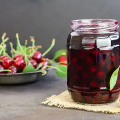 Słoik pełen słodkich wiśni w syropie, obok talerz świeżych owoców. Idealne na deser.