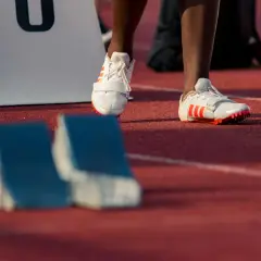 Białe buty sprintera z pomarańczowymi paskami, gotowe do startu na bieżni.