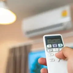 Mano sujetando control remoto para aire acondicionado, ajustando temperatura. Mantenimiento aire acondicionado para confort.