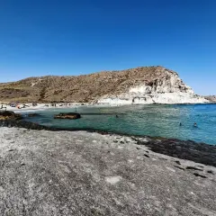Gente disfrutando del sol y el mar en la cala de enmedio almeria, con aguas cristalinas y formaciones rocosas.