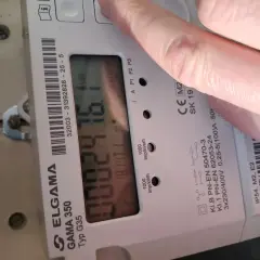 Dłoń naciska przycisk licznika energii elektrycznej ELGAMA GAMA 350. Wyświetla się zużycie 0082476.1 kWh.