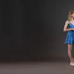 Dwie młode kobiety przy pulpicie z nutami. Jedna w niebieskiej sukience, druga w białej bluzce i różowej spódniczce. Przygotowują się do kursu wokalnego.