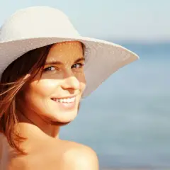 Frau mit Hut am Strand, genießt die Sonne mit Sonnencreme LSF 50 Gesicht.