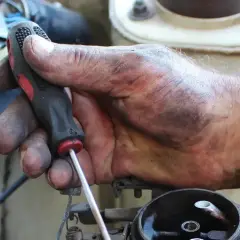Brudna ręka mechanika przykręca śrubę podczas wymiany linki hamulca ręcznego.