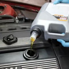 Ręce w niebieskich rękawiczkach wlewają olej silnikowy Liqui Moly do silnika. Czy można mieszać oleje silnikowe? To pytanie nurtuje wielu kierowców.