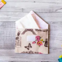 Sobres de tela con diseño de París y flores, junto a carretes de hilo, cinta métrica y descosedor.