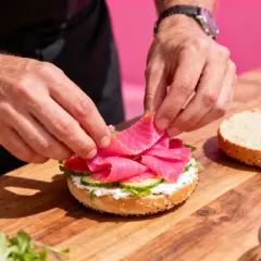 Préparation d'un bagel garni de saumon fumé, de fromage frais et de concombre. Un accompagnement bagel parfait pour un brunch.