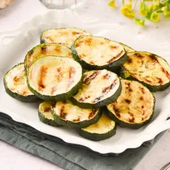 Rodajas de calabacín a la plancha, con marcas de parrilla doradas, servidas en un plato blanco festoneado.