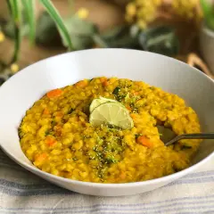 Un tazón de lentejas al curry con zanahoria y calabacín, decorado con rodajas de lima y ralladura.