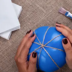 Ręce trzymają niebieski balon owinięty sznurkiem. Obok leżą białe serwetki i pędzel. To początek tworzenia zabawki sensorycznej.