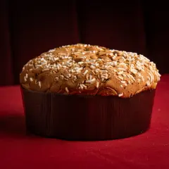 Un panettone tradicional, uno de los tipos de panettone, cubierto con azúcar perlado y almendras, sobre un mantel rojo.