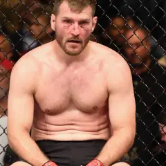 Stipe Miocic, med blodiga sår i ansiktet, sitter utmattad i buren efter en tuff match.