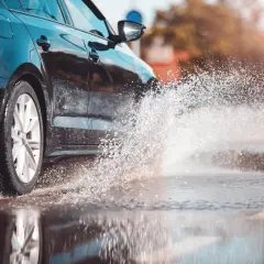 Coche negro salpicando agua. Para evitar el aquaplaning, reduce la velocidad y mantén tus neumáticos en buen estado.