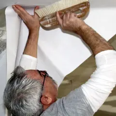 Mann tapeziert die Decke mit einer Bürste, um die Tapete glatt zu streichen.